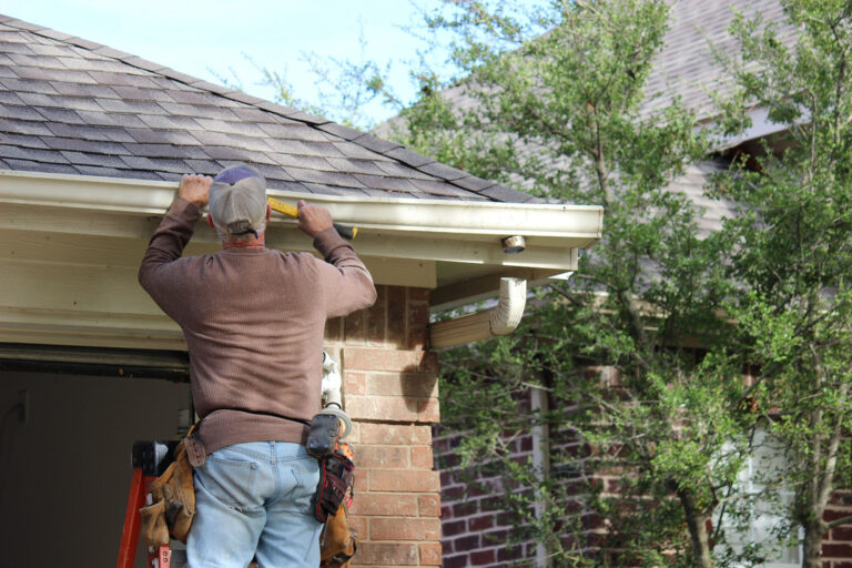 Installing roof gutters; Worker Attaching Aluminum Rain Gutter and Down Spout; Contractor installing gutters on a residential building